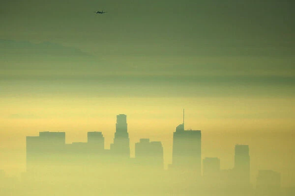 Downtown Los Angeles and an airplane are seen through the morning marine layer in
