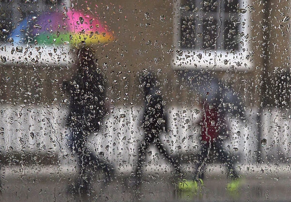 Family is seen through raindrops on a window as they shelter under umbrellas during a