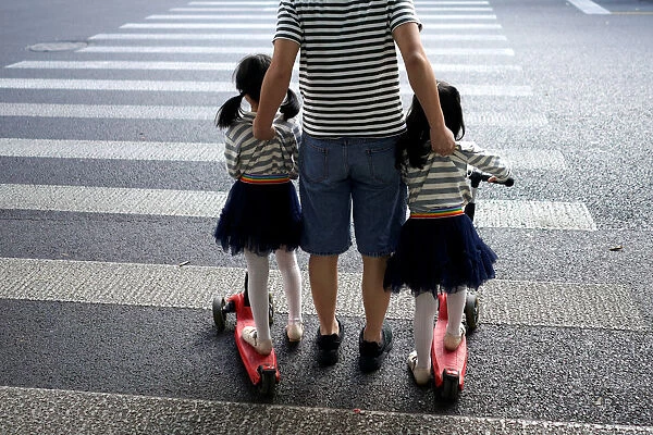 A father crosses a road with his twin daughters in Shanghai