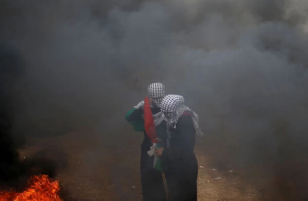 Female Palestinian demonstrators stand amidst smoke during a protest demanding the right