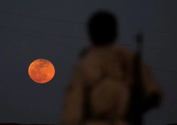 A fighter from Free Syrian Army is seen watching a full moon rises in Daraa