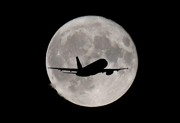 FILE PHOTO: A passenger plane passes in front of the full moon as it makes its final