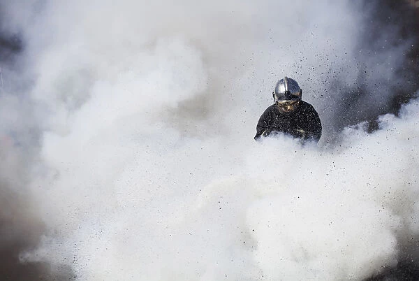 A firefighter is engulfed by white smoke while extinguishing burning tyres during