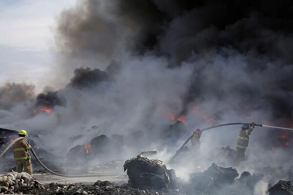 Firefighters work to extinguish the fire as it burns through a pile of old tyres at a