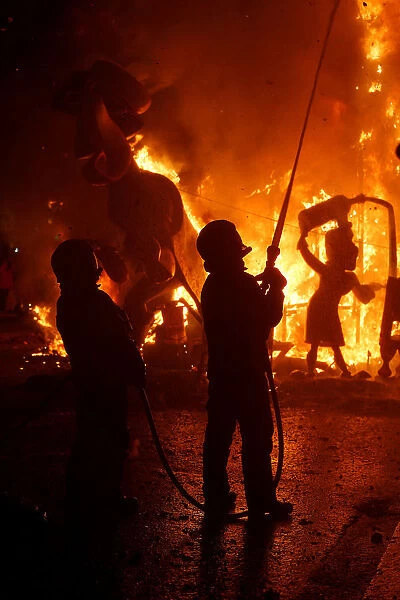 firemen spray water at figures of a monument as it burns during the finale of the Fallas