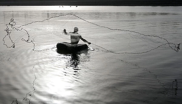 Fisherman floating on a rubber tube throws a net to catch fish from the waters of the