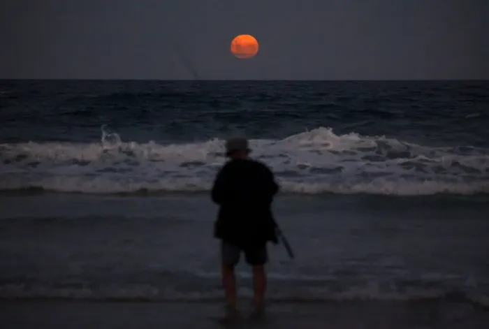 Framed Print : A fisherman prepares to cast his line standing in the surf as a full moon rises Framed Print : A fisherman prepares to cast his line standing in the surf as a full moon rises