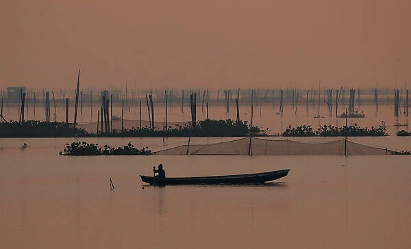 A fisherman rows his canoe as he inspects a fish cage at Laguna de Bay in Muntinlupa