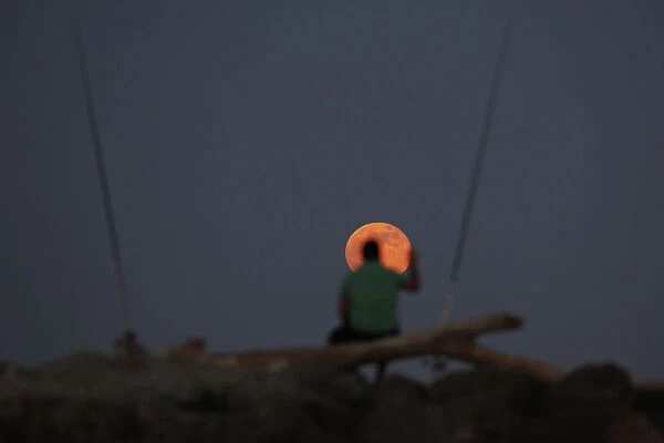 A fisherman waits for a catch as a super moon rises over Guadalmar beach in Malaga