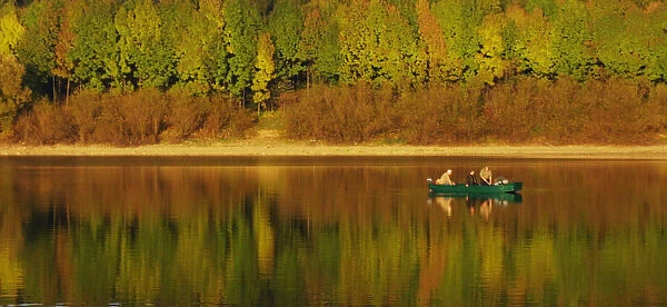 FISHERMEN IN BOAT ARE CAMOUFLAGED BY COLOURS OF FALL AT DAM IN SLOVAKIA