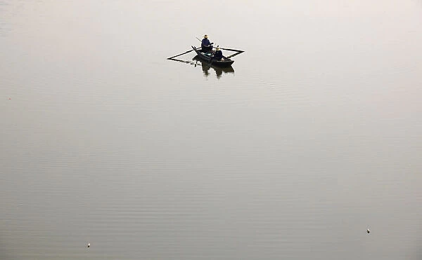 Fishermen row a boat in the knee-deep Neijing River near the city of Honghu in central