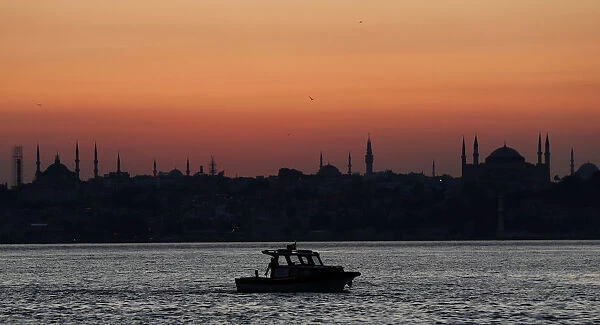 A fishing boat sails in the Bosphorus as the sun sets over the old city in Istanbul