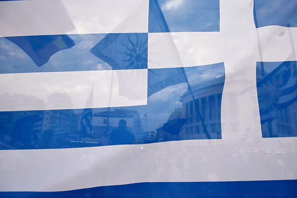 A flag depicting Vergina sun is seen through a Greek flag during a demonstration against