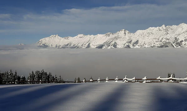 Fog covers the Inntal valley in front of snow covered mountain summits in Tulfes