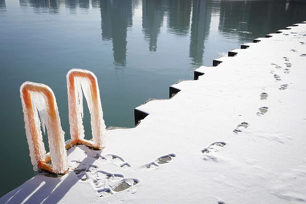 Footprints can be seen along the ice covered shore as the reflection of the skyline