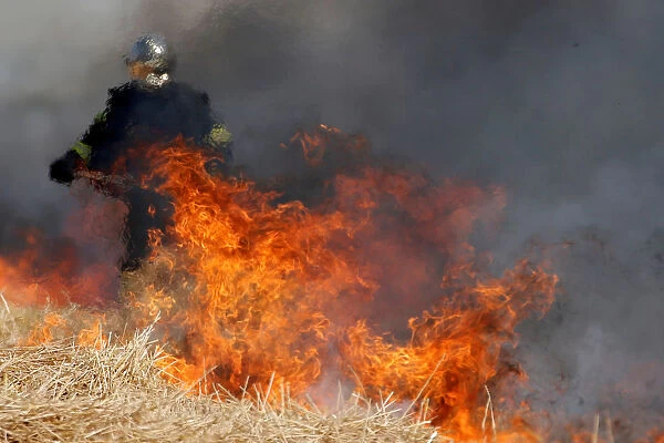 A French fireman uses a shovel behind flames in a burning field of barley during harvest