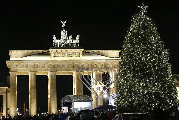 A giant menorah stands next to a Christmas tree in front of the Brandenburg gate to