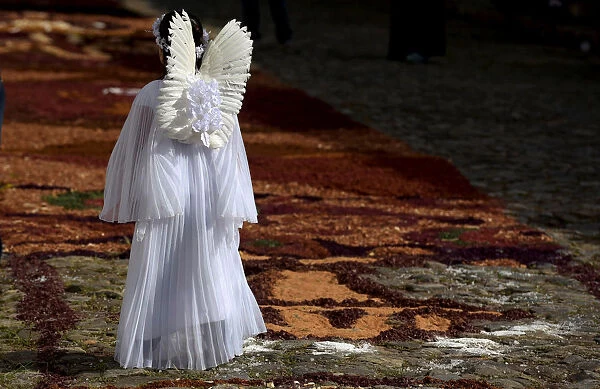 A girl dressed as an angel walks in the middle of a street decorated by residents