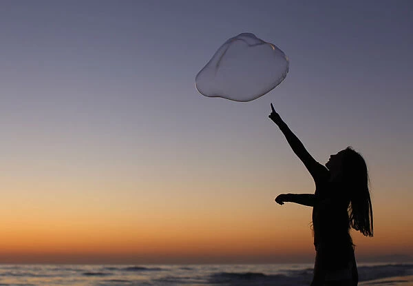 A girl plays with a giant bubble as the sun sets at Moonlight Beach in Encinitas