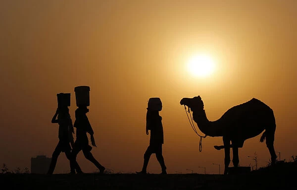 Girls carrying buckets filled with water are silhouetted against the setting sun as
