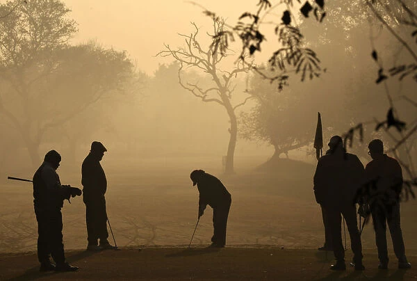 A golfer is silhouetted against the rising sun as he prepares to hit a shot during