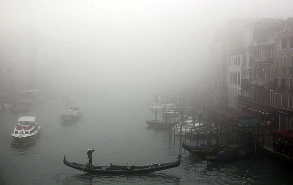 A gondolier rows his gondola across the Grand Canal in the fog in Venice