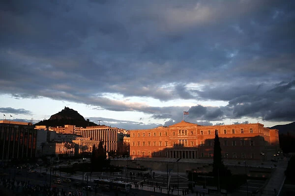 A Greek national flag flutters atop the parliament building during sunset in Athens