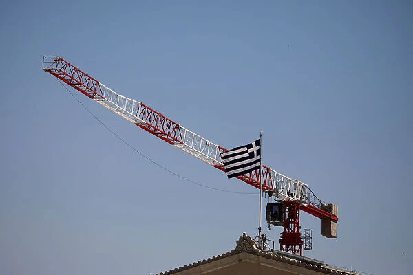 A Greek national flag flutters atop the parliament building as a construction crane is