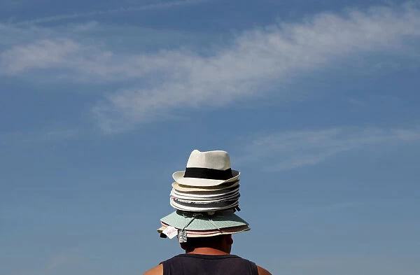 A hat seller wears his merchandise on his head as he tries to sell hats to tourists