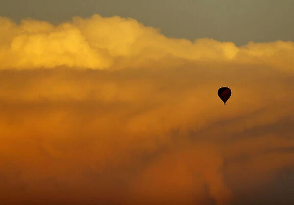 A hot air balloon floats past a distant thunderstorm after sunset near San Diego