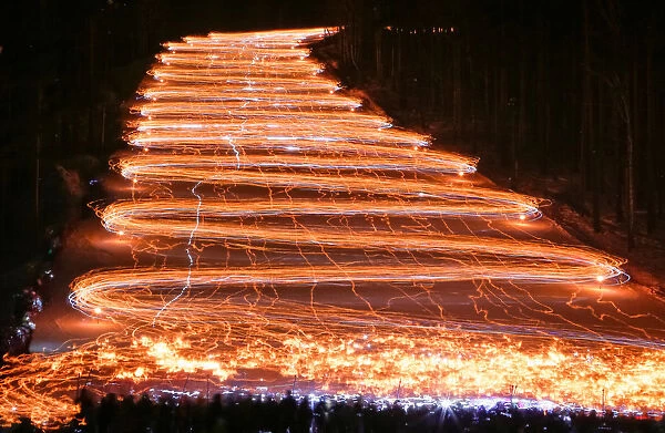 Hundreds of skiers and snowboarders descend from a slope while holding lit torches
