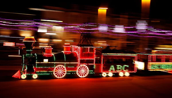 An illuminated tram in the shape of a steam locomotive passes under the illuminations