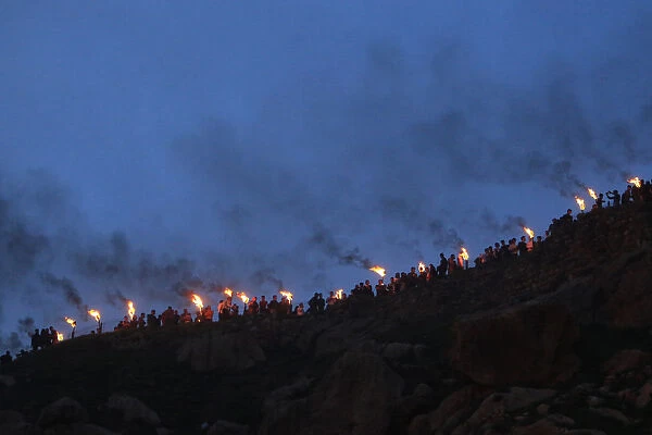 Iraqi Kurdish people carry fire torches up a mountain, as they celebrate Newroz Day