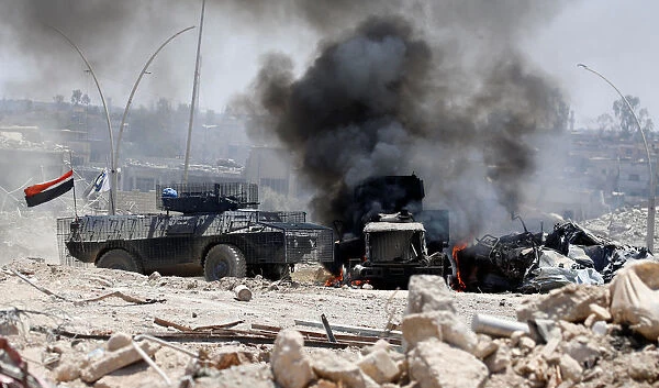 An Iraqi military armoured fighting vehicle (AFV) drives past a burning Iraqi military
