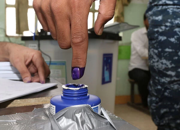 An Iraqi security member dips his finger in ink after casting his vote at a polling