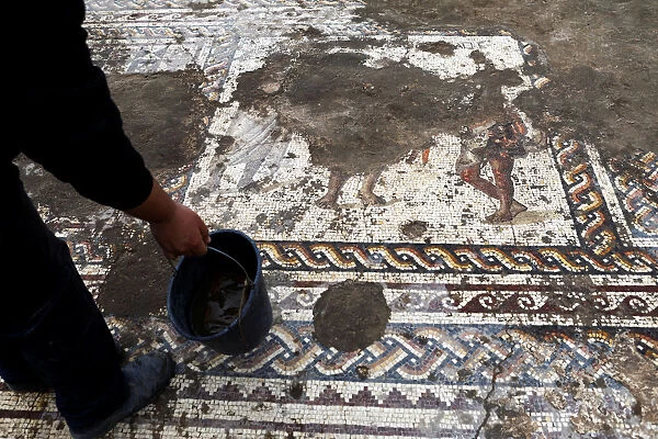 An Israel Antiquities Authority worker holds a bucket while cleaning a mosaic floor