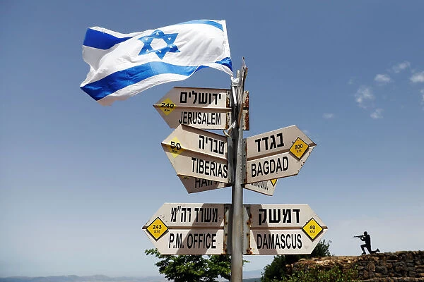An Israeli flag is seen on top of signs pointing out distances to different cities
