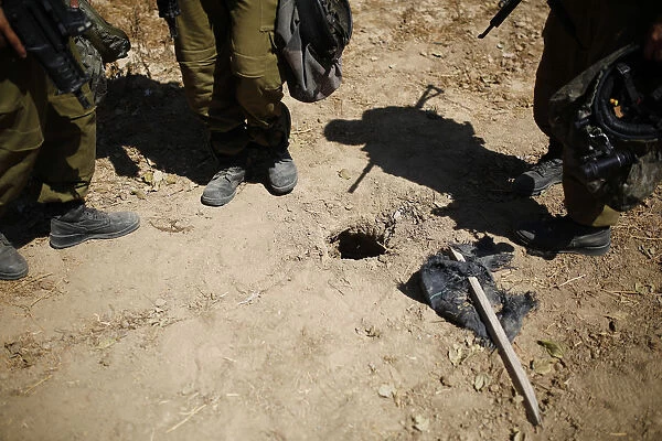 Israeli soldiers stand next to a hole in the ground they suspect is connected to a tunnel