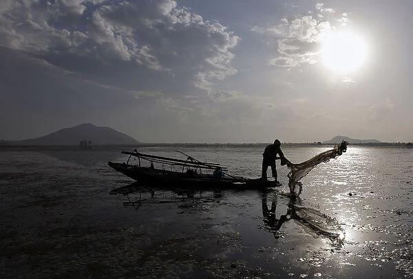 A Kashmiri fisherman throws a net into the waters of the Dal Lake in Srinagar