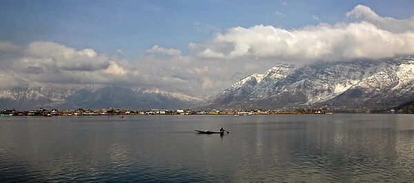 Kashmiri man rows boat on Dal Lake surrounded by snow-covered mountains in Srinagar