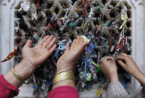 A Kashmiri Muslim woman prays as another one ties a thread on the window of the shrine of