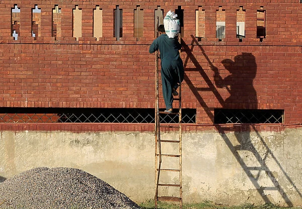 A laborer carries a sack of gravel up a ladder to the roof of a house under construction