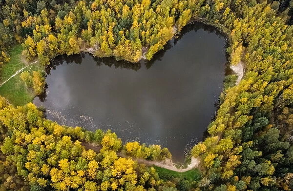 A lake in a shape of a heart is seen surrounded by autumn-coloured trees outside