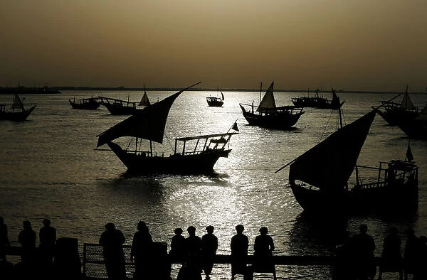 Locals watch traditional fishing boats as they sail past the heritage village during the