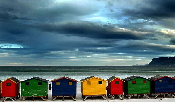 LONE STROLLER STANDS BY BEACH HUTS IN CAPE TOWN
