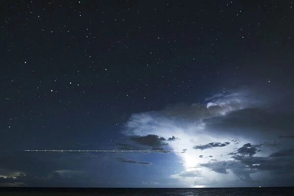 A long exposure shot shows a plane flying over the sea during a lightning storm on the