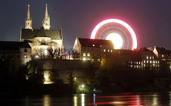 A long time exposure shows a ferris wheel turning beside Basels landmark the Muenster