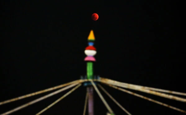 A lunar eclipse of a full Blue Moon is seen rising over a roller coaster ride in
