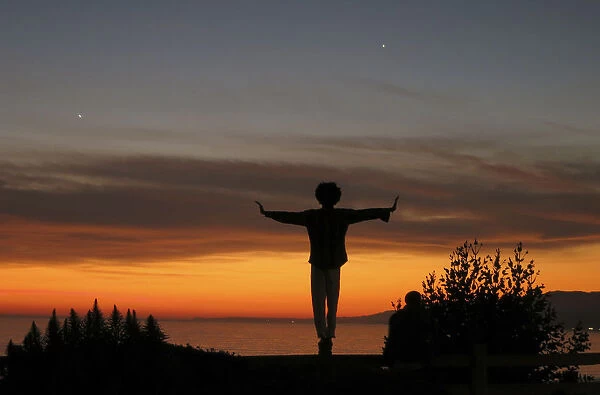 A man balances on a fence post as he watches the sun set over the Pacific Ocean in Santa