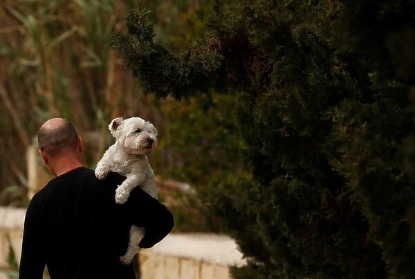 A man carries his pet dog while walking in Marsaxlokk